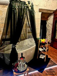 a bath tub in a room with a table with wine glasses at Escapade Romantique in Les Roches-lʼÉvêque