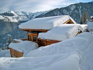 a cabin covered in snow with mountains in the background at Chalet Chocolat in La Tzoumaz