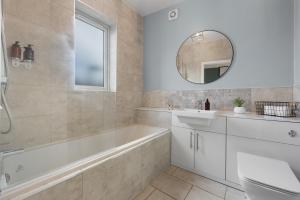 La salle de bains est pourvue d'une baignoire, d'un lavabo et d'un miroir. dans l'établissement 4-BR Chic Spacious House with Parking, Central Bolton, Links to Manchester, Sleeps - 11 by Blue Puffin Stays, à Farnworth