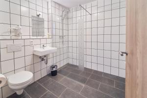 a white tiled bathroom with a toilet and a sink at Hotel am Interpark in Großmehring