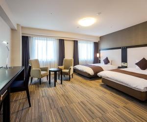 Daiwa Roynet Hotel Oita في أويتا: غرفة فندقية بسريرين ومكتب وكراسي