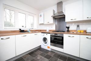 cocina con armarios blancos, lavadora y secadora en Buxton Way by Tŷ SA - 3 bedroom house, en Royal Wootton Bassett