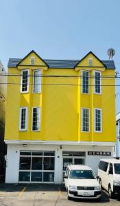 a yellow building with two cars parked in front of it at Warm House6 in Sapporo