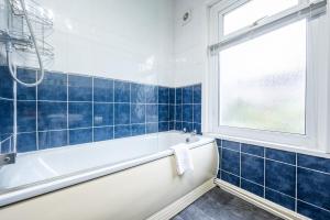 a blue tiled bathroom with a tub and a window at Dos Road by Tŷ SA in Newport