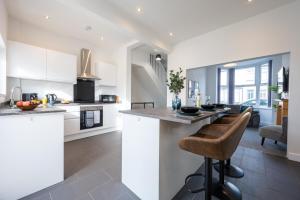 a kitchen with white cabinets and a bar with stools at Durham View by Tŷ SA in Newport