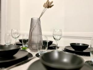 une table avec des verres et un vase avec une fleur dans l'établissement Serviced 4 bed 2 bath Manor Park House, à Londres