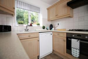 a kitchen with wooden cabinets and a white dishwasher at Langstone Close by Tŷ SA in Llanwern