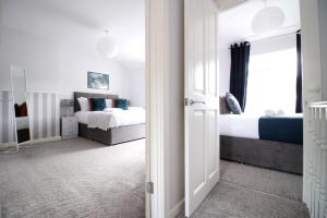 a white bedroom with two beds and a window at Willow Way by Tŷ SA in Nantgarw