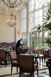 a man standing in a restaurant with tables and chairs at Waldorf Astoria Versailles - Trianon Palace in Versailles