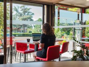 una mujer sentada en una mesa con un portátil en ibis Colmar Est - Hotel Restaurant en Alsace en Colmar