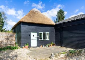 a black shed with a thatched roof and a white door at Little Barn in Upton