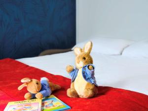 two stuffed animals sitting on a bed with a book at Mercure Chartres Cathedrale in Chartres