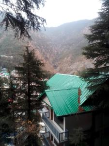 a building with a green roof with mountains in the background at Himalayan Mountain View, Triund Trekking Hostel in Dharamshala