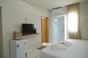 Dieses weiße Zimmer verfügt über ein Bett und einen TV. in der Unterkunft Pousada Garden das Flores in Chapada dos Guimarães