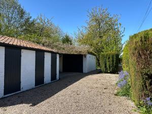 a garage with a white building and some trees at Charming converted Granary in Capelle-lès Hesdin