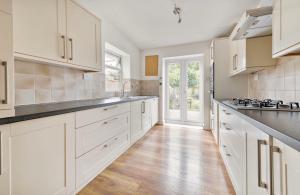 a kitchen with white cabinets and a wooden floor at Calderon Road in London