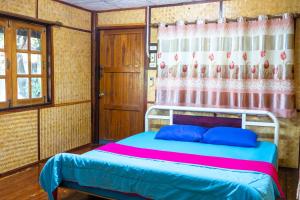 a bedroom with a bed with blue pillows and a curtain at Ruenpakkiangnan เรือนพักเคียงน่าน in Phitsanulok