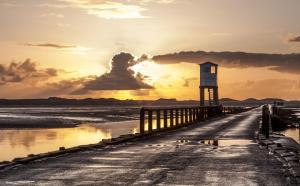 a lighthouse on a pier with the sunset in the background at Mill Cottage, Brockmill Farm in Berwick-Upon-Tweed