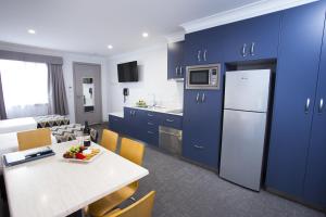 una cocina con armarios azules y una mesa con un bol de fruta en Altitude Motel Apartments, en Toowoomba