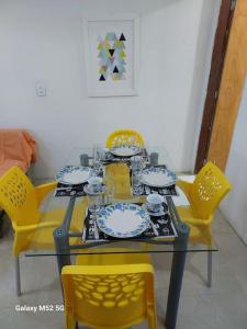 a dining table with yellow chairs and a table with dishes on it at Studio com varanda - Melhor localização do Arruda in Recife