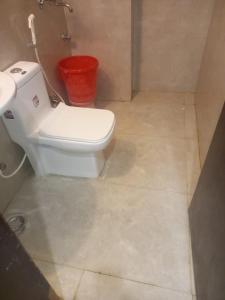 a bathroom with a toilet and a red bucket at Hotel First by Goyal Hoteliers in Agra