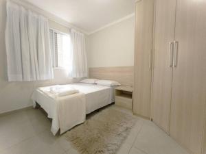 a white bedroom with a bed and a window at Charmoso Apto com Vaga Ar AM206 in Maringá