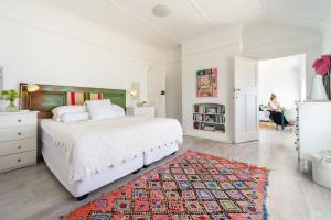 un dormitorio blanco con una cama y una mujer sentada en una silla en Kalimera Beach House, en Mossel Bay