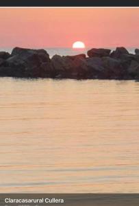 een zonsondergang boven een waterlichaam met rotsen bij 1era linea de playa Cullera Villa Sales in Cullera