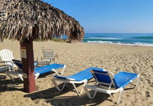 Oceanview Penthouse on the Beach في كاباريتي: مجموعة من الكراسي ومظلة على الشاطئ