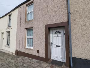 un edificio con una puerta blanca y dos ventanas en Foxy Lady Cottage, en Workington