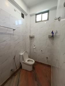 a white bathroom with a toilet and a window at Ujjayanta Homestay in Agartala