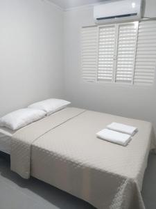a white bedroom with a bed with two towels on it at My House Hospedagem in Santo Ângelo