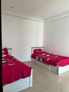 2 bedden in een witte kamer met rode lakens bij Appartement spacieux en bord de mer in Temara