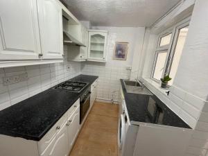 Double Room في Morden: مطبخ مع خزائن بيضاء وقمم منضدة سوداء