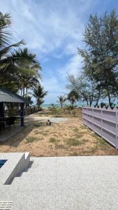 a white fence on a beach with trees and the ocean at SR Tiny House in Bachok