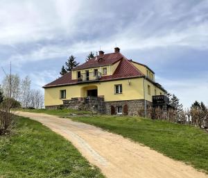 a large yellow house on a hill with a dirt road at Apartament Karkonoska in Przesieka