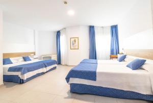 two beds in a hotel room with blue curtains at Hotel Pozo del Duque II in Zahara de los Atunes