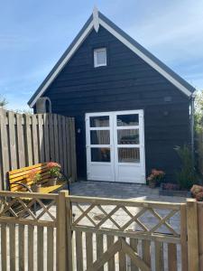 a black house with a white door and a wooden fence at gezellige cottage in zeeland in Sint Annaland