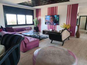 sala de estar con muebles de color púrpura y TV de pantalla plana. en Dar illy, en Bir Jedíd Saint-Hubert