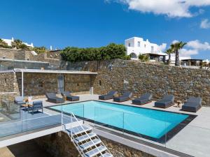 - une piscine avec des chaises longues à côté d'un mur en pierre dans l'établissement Stunning Oceanview Mykonos Villa | 5 Bedrooms | Villa Perseus | Amazing Location Overlooking Sea & Private Pool | Faros, à Fanari