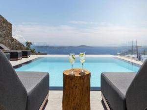 two wine glasses sitting on a stump next to a swimming pool at Stunning Oceanview Mykonos Villa | 5 Bedrooms | Villa Perseus | Amazing Location Overlooking Sea & Private Pool | Faros in Fanari