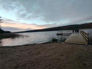 dos personas de pie en un muelle cerca de un lago en Klimatyczny domek w lesie przy jeziorze en Gietrzwałd