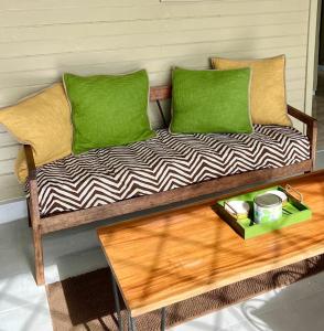 a wooden bench with two green pillows and a table at Adella's Blue Mountain Coffee Farmstay in Kingston
