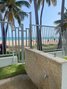 a beach with a fence and palm trees and the ocean at Beachfront Bliss at Isla Verde in San Juan