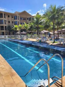 a large swimming pool with palm trees and a hotel at Apartamento com varanda Reserva do Sahy in Mangaratiba