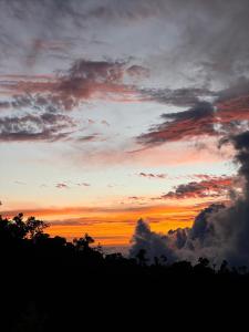 einen Sonnenuntergang mit Wolken und Bäumen im Vordergrund in der Unterkunft Mario's Lodge Providencia in Copey