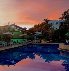 - une piscine en face d'une maison avec un coucher de soleil dans l'établissement Hotel Fazenda Tucano, à Capim Branco