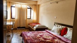 a bedroom with two beds and a table and two windows at Goroomgo Naina Homestay Near By Landour Clock Tower Mussoorie in Mussoorie