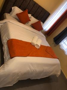 Bett mit orangefarbener und weißer Bettwäsche und Kissen in der Unterkunft Hosted by Noel in Naivasha