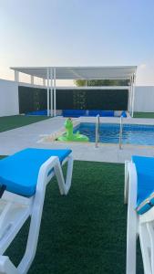 uma piscina com duas cadeiras azuis e brancas ao lado de uma piscina em Falaj Hub Retreat em Umm Al Quwain